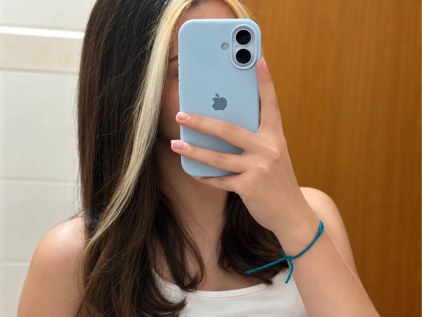 Foto atual de Lara em frente ao espelho segurando um celular azul
